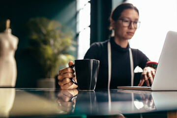 Female dressmaker working on laptop with cup of coffee