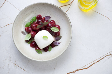 Plate with mozzarella, sweet cherry and fresh basil over light-beige marble background, horizontal shot with copyspace, above view