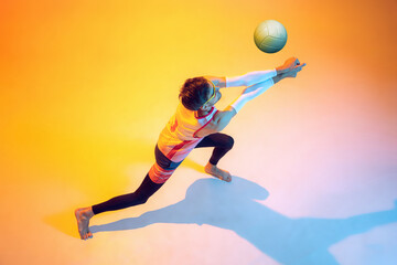 Portrait of young man, volleyball player in motion, kicking ball, playing isolated over yellow...