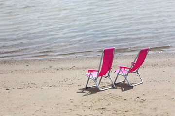 Fototapeta na wymiar two chaise longues on a beach near waterline two chaise longues on a beach near waterline