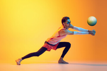 Portrait of young man, beach volleyball player in motion, training, playing isolated over yellow studio background in neon light