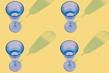 Blue wine glass with sharp shadow flat lay seamless pattern on pastel yellow background. Birthday celebration party greeting card or wallpaper idea.