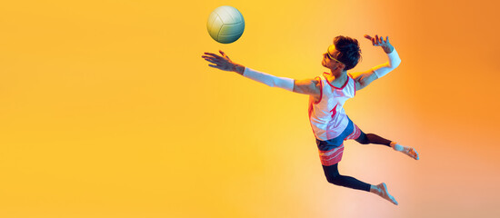 Fototapeta na wymiar Young man, beach volleyball player in motion, training, servig ball in jump isolated over yellow studio background in neon light. Flyer