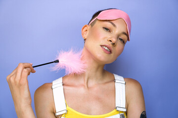 Sexy pierced woman wearing sleep mask touching her neck with erotic feather