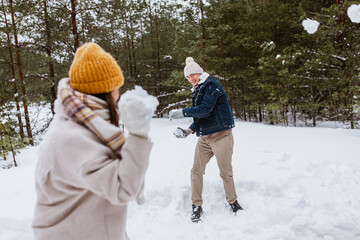 people, season and leisure concept - happy couple playing snowballs in winter park