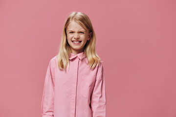 Fototapeta premium a little girl of school age stands in a pink shirt on a pink background with a very angry face