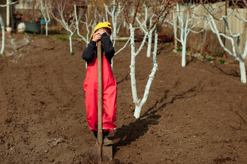 a child in a red jumpsuit is digging the ground in the garden. the boy helps in the garden to plant seedlings