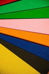 Abstract background made of corrugated paper for application. Space for text. Texture. Sheets of different colors lie in a fan. Green, red, blue, black, pink, orange color.