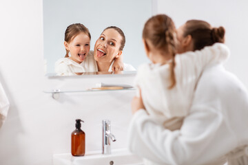 Obraz premium beauty, family and people concept - happy smiling mother and little daughter looking to mirror and hugging in bathroom