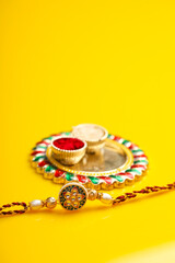 Indian festival raksha bandhan: puja thali and rakhi or wrist band on yellow background.