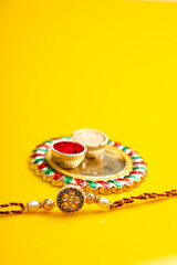 Indian festival raksha bandhan: puja thali and rakhi or wrist band on yellow background.