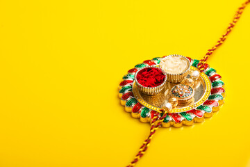 Indian festival raksha bandhan: puja thali and rakhi or wrist band on yellow background.