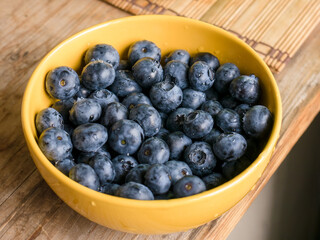 Washed blueberries (Vaccinium uliginosum) in a yellow bowl on a wooden table