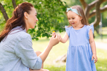 family, motherhood and people concept - happy mother with little daughter with flowers at summer park or garden