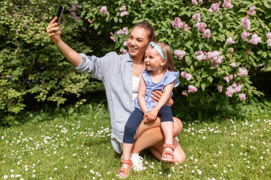 family, motherhood and people concept - happy mother and little daughter with smartphone taking selfie at summer park or garden
