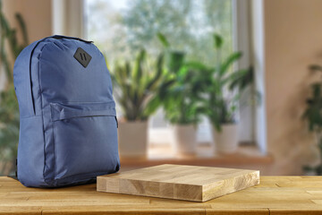 Schoolbag on table and blurred window with green plants. 