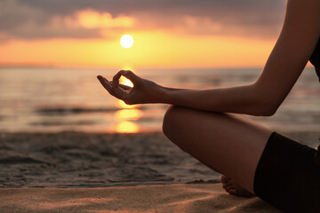 yoga, mindfulness and meditation concept - close up of woman meditating in lotus pose on beach over...