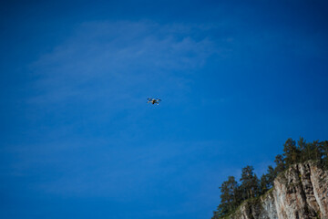 Quadcopter flies in the sky on a blue background, the flight of a small quadcopter in the mountains video shooting from a bird's eye view, a flying drone