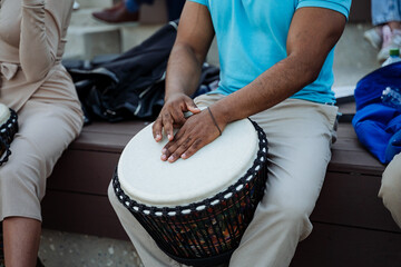 The black hands of an African-American play ethnic music on a djemba, a leather-covered plastic drum, an African musical instrument.