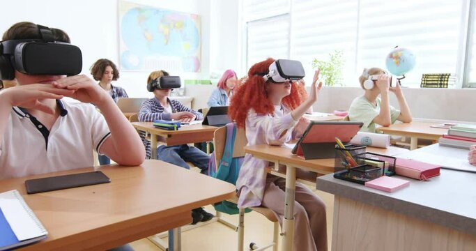 Smart Pupils Wearing VR Headsets And Studying With Future Technologies At Classroom. Excited Boys And Girls In Virtual Glasses Experienced Augmented Reality At Lesson In School.