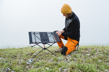 The guy collects a frame table for camping in nature, assembling camping equipment, picnic in the mountains, fog.