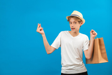 Surprised caucasian guy holding a shopping bags in his hand. Studio shot on blue wall.