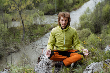 Meditation on the mountain, yoga in nature, the guy sits in the lotus position, time alone with himself, chinmudra on his fingers, a curly hipster practices hatha yoga.
