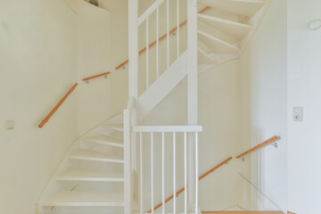 From above of narrow spiral stairway with white stairs and railing on wall inside of modern...