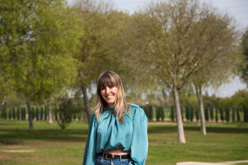 beautiful young blonde woman dressed in jeans and boots is walking in the park and is having her photo taken while enjoying the sunny spring day in europe. Holiday and free time concept.