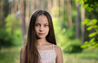 Portrait of beautiful preteen girl in forest with pine-trees on summer sunset outdoors