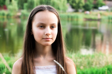 Portrait of beautiful preteen girl against lake on summer cloudy day outdoors