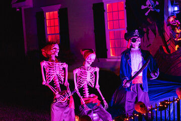 A set of skeletons and a pirate skeleton outside a haunted house on Halloween night in October