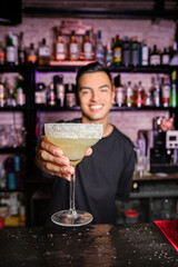 unfocused young waiter shows a margarita cocktail on camera in the foreground