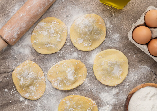 Uncooked stuffed raviolonis or raviolis with flour over wooden table