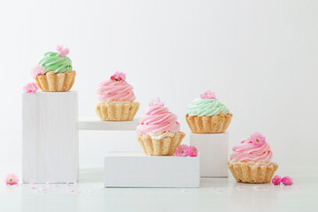 pink and green cupcakes with spring flowers  on wooden podiums on white  background