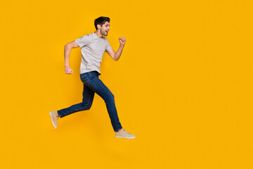 Fototapeta na wymiar Full body profile photo of funny brunet millennial guy run wear t-shirt jeans sneakers isolated on yellow background