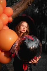 Naklejka premium Portrait of a beautiful woman in a witch costume holding a black ball in her hands. Halloween