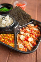Salmon pickled in soy sauce or shoyu sauce and sprinkled with chili and sliced garlic. with spicy sauce Seaweed and Japanese rice are side dishes on a brown wooden table.