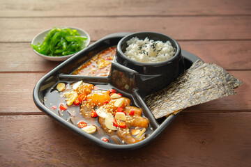 Salmon pickled in soy sauce or shoyu sauce and sprinkled with chili and sliced garlic. with spicy sauce Seaweed and Japanese rice are side dishes on a brown wooden table.