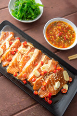 Salmon pickled in soy sauce or shoyu sauce and sprinkled with chili and sliced garlic. with spicy sauce Seaweed and Japanese rice are side dishes on a brown wooden table.
