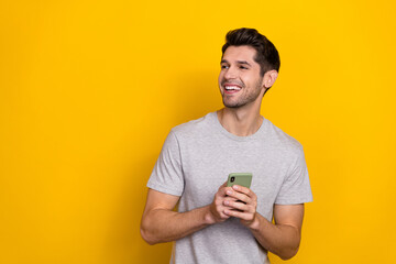 Photo of impressed brunet millennial guy hold telephone look promo wear trend cloth isolated on yellow color background