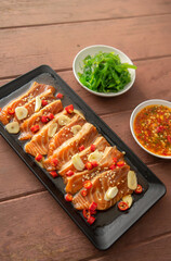 Salmon pickled in soy sauce or shoyu sauce and sprinkled with chili and sliced garlic. with spicy sauce Seaweed and Japanese rice are side dishes on a brown wooden table.