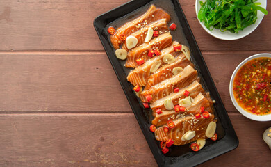 Salmon pickled in soy sauce or shoyu sauce and sprinkled with chili and sliced garlic. with spicy sauce Seaweed and Japanese rice are side dishes on a brown wooden table.