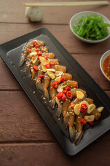 Prawns pickled in soy sauce or shoyu sauce and sprinkled with chili and sliced garlic with spicy sauce Seaweed and Japanese rice are side dishes on a brown wooden table.