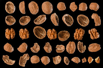 Walnut shells, cracked pieces of shell, walnut kernels different size of walnuts and shells in symmetrically lined on black background.