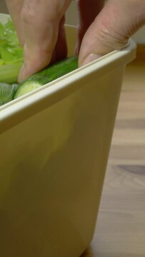 Vertical video social media format &ndash; Closeup of a hand opening the lid of a kitchen composting bin, which is nearly full of vegetable waste, then adding a piece of cucumber and shutting the lid.