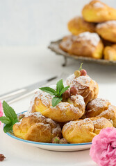 Baked eclairs with custard cream on a metal round plate sprinkled with powdered sugar