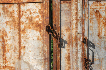An old iron gate with a forged iron chain. An old rusty gate closed with a chain and a padlock.