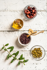 Olive pate in ramequin bowl and basic ingredients on white wooden background with olive branch. Flat lay