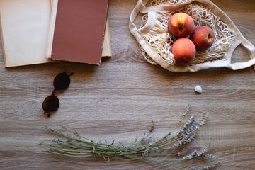 Sunglasses, vintage books, reusable mesh bag with fresh peaches, seashell and lavender flowers on wooden background Boho and rustic summery details, flat lay.